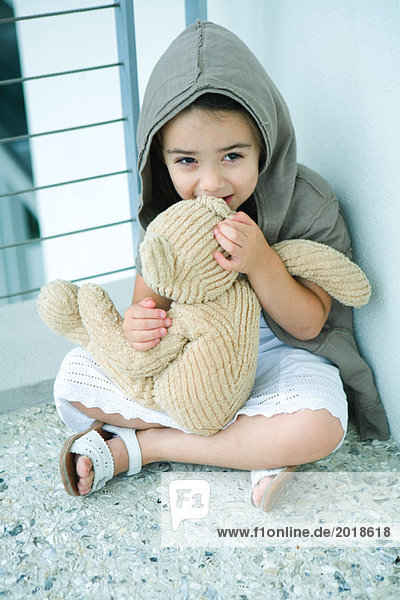 Kleines Mädchen auf dem Boden sitzend  flüsternd in das Ohr des Teddybären  volle Länge