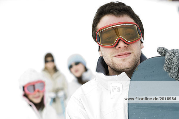 Young man standing with snowboard  friends in background  portrait