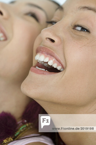 Zwei junge Freundinnen lachend  eine schaut in die Kamera  extreme Nahaufnahme von Gesichtern  beschnitten