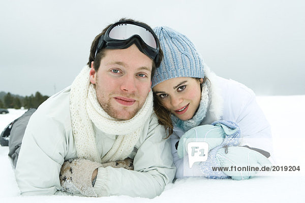 Young couple lying side by side in snow  smiling at camera  portrait