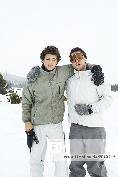 Two young skiers standing with arms around each other's shoulders  smiling at camera  portrait