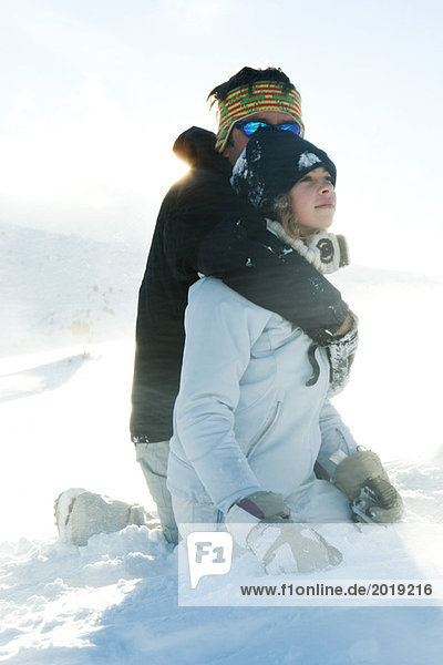 Mature man embracing teenage girl  both kneeling in snow
