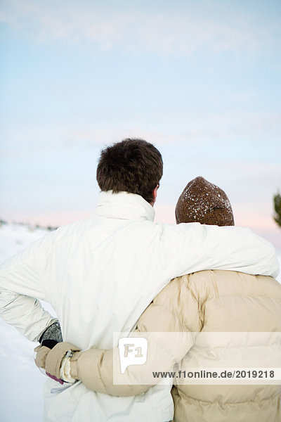 Two unrecognizable people standing together  embracing  dressed in winter clothing  rear view