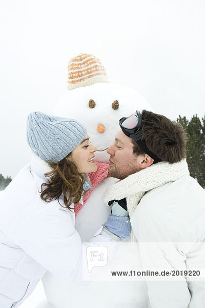Young couple leaning towards each other in front of snowman  smiling  portrait