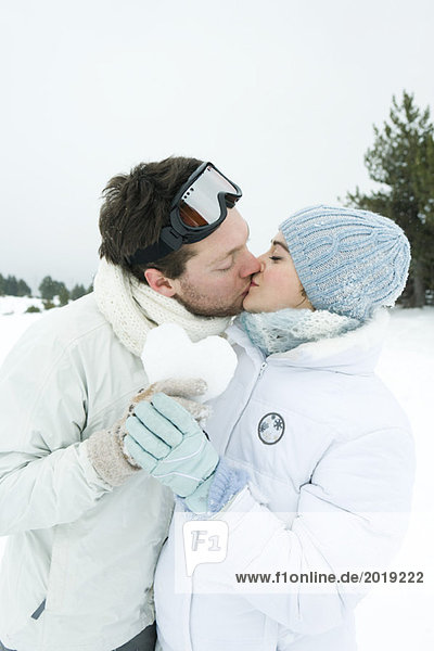 Young couple kissing  holding heart made of snow together  eyes closed  portrait