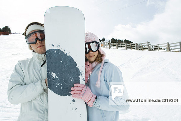 Teenagerin und junger Mann stehen zusammen  halten Snowboard  lächeln in die Kamera  Porträt