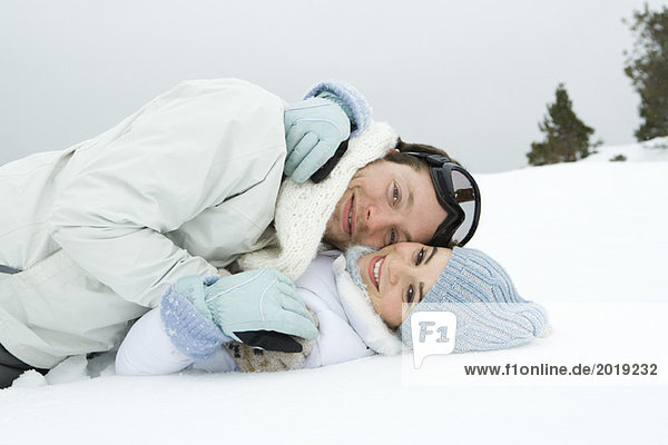 Young couple reclining together in snow  smiling  portrait