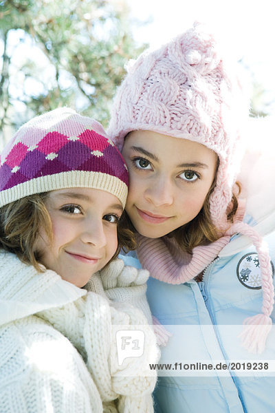 Two sisters smiling at camera  cheek to cheek  both wearing knit hats  portrait