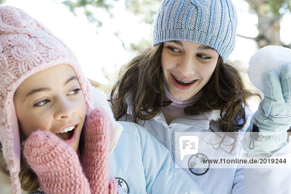 Zwei Teenagermädchen lächelnd  eines mit Schneeball  beide in Winterkleidung.