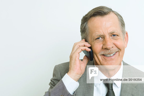 Senior businessman using cell phone  smiling at camera  portrait