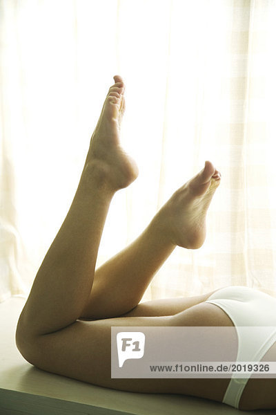 Junge Frau auf dem Bauch liegend in Unterwäsche mit hochgezogenen Beinen