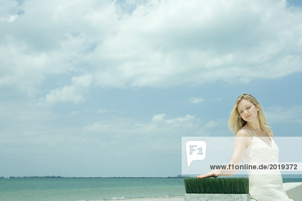 Woman sitting near sea  touching blades of wheat grass