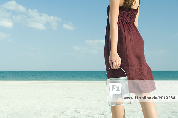 Woman standing on beach  holding bucket  cropped  rear view