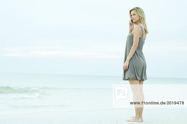 Young woman standing on beach  using cell phone  looking away