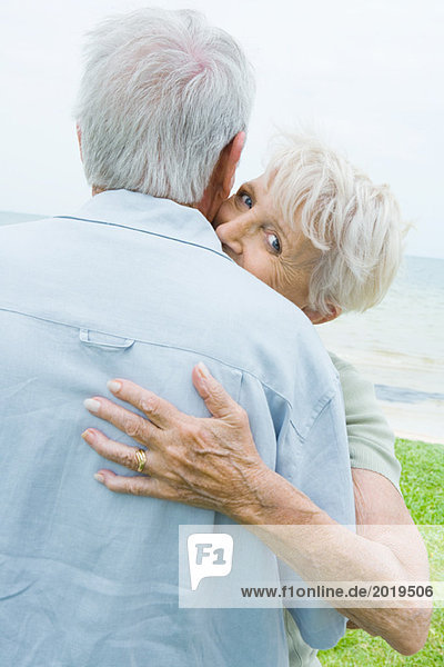 Seniorenpaar umarmt  Frau schaut über die Schulter des Mannes zur Kamera