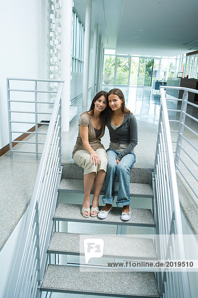 Mutter und Teenagermädchen zusammen  auf Stufen sitzend  lächelnd vor der Kamera  volle Länge