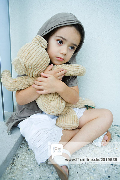 Kleines Mädchen auf dem Boden sitzend  umklammernder Teddybär