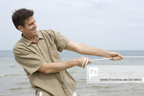 Mann zieht Seil  lächelnd  Ozean im Hintergrund  Taille oben