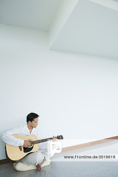 Young man sitting on floor  playing guitar  full length