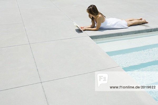 Woman in sundress lying by edge of pool  reading  full length