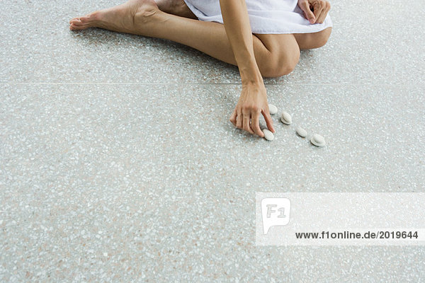 Frau kniend auf dem Boden  Kieselsteine in einer Linie platzierend  abgeschnitten  hohe Winkelansicht