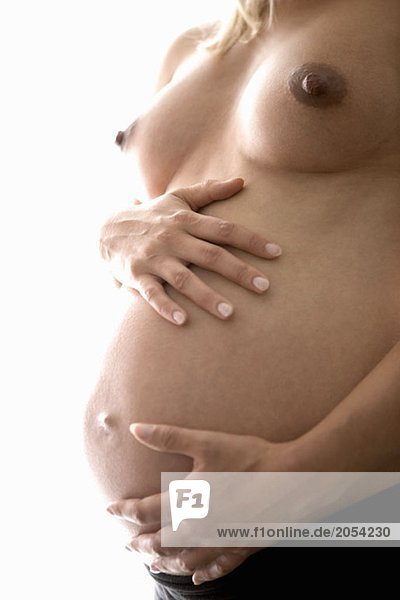 Mittelteil einer hemdlosen schwangeren Frau  die ihren Bauch berührt