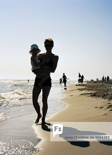 Silhouette of a woman holding a young boy whilst walking on a beach