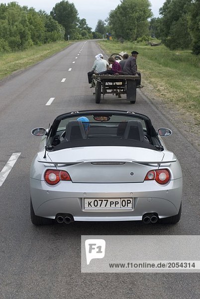 A sports car driving behind a horse cart on a road