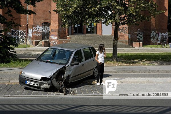 Eine junge Frau steht neben einem beschädigten Auto.