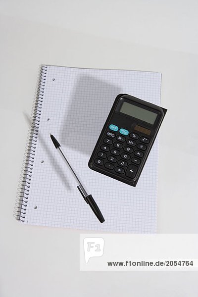Ein Taschenrechner und ein Stift schweben über dem Notizbuch