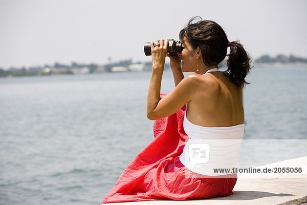 Side view of a woman using binoculars by the sea