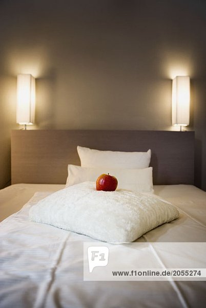 Ein roter Apfel auf einem weißen Kissen auf einem Bett