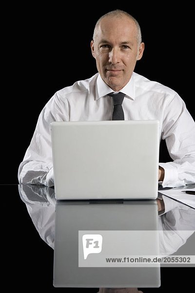 Ein Geschäftsmann  der hinter seinem Laptop sitzt.