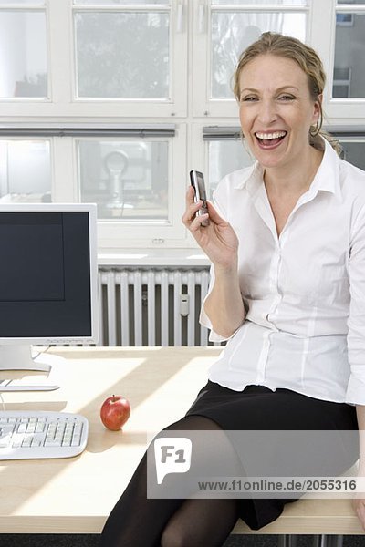 Eine Geschäftsfrau sitzt auf ihrem Schreibtisch und lacht.