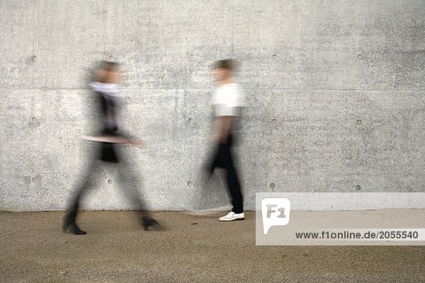 Zwei Menschen die an einer Mauer vorbeigehen.