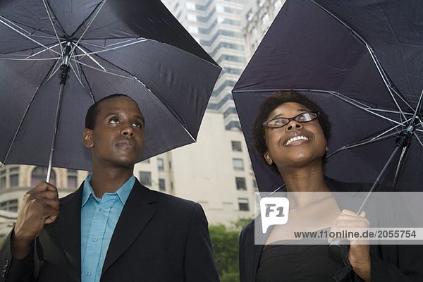 Man and woman downtown  each standing under an umbrella