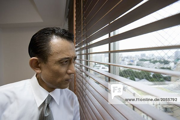 A businessman looking through window blinds