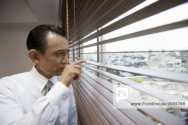 A businessman looking through window blinds