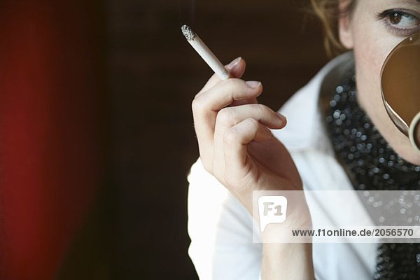 Eine Frau sitzt rauchend im Café und trinkt einen Kaffee