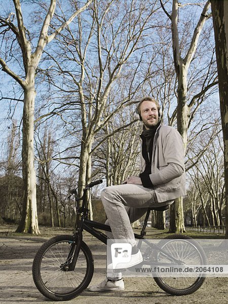 A man wearing headphones and sitting on a BMX in a park