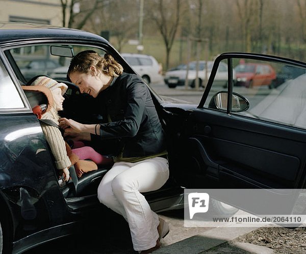 A woman putting a safety belt on her daughter