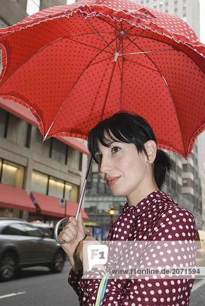 Junge Frau in einem gepunkteten Kleid mit einem gepunkteten Schirm auf einer Straße  New York City
