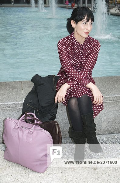 Junge Frau sitzt mit ihrem Gepäck in der Nähe eines Springbrunnens  New York City