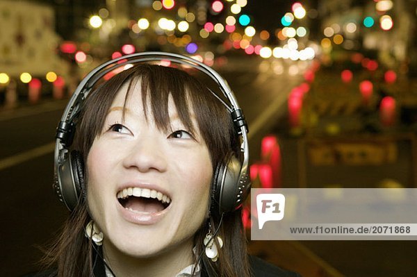 Eine junge Frau hört auf einer Straße stehend Musik über Kopfhörer  Tokio  Japan