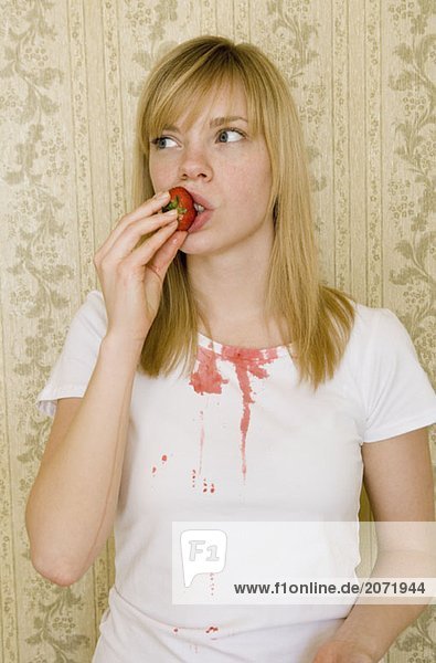 Eine junge Frau isst eine Erdbeere und bekleckert ihr T-Shirt