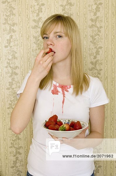 Eine junge Frau isst eine Erdbeere und bekleckert ihr T-Shirt