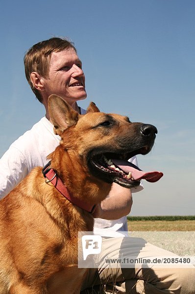 Man sitzt mit Hund im Feld