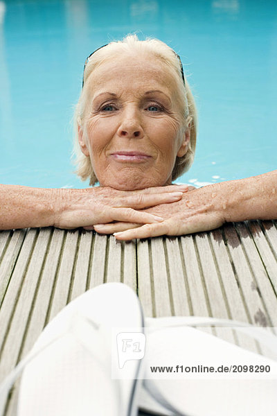 Germany  Senior woman resting on edge of pool  smiling