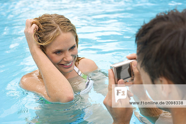 Junger Mann fotografiert Frau im Pool
