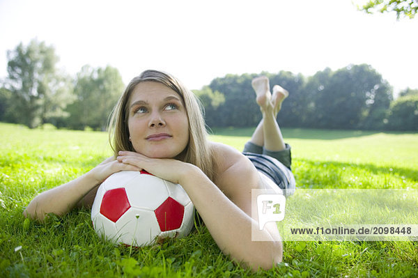 Frau (20-25) im Feld liegend  auf Fußball gestützt  Nahaufnahme